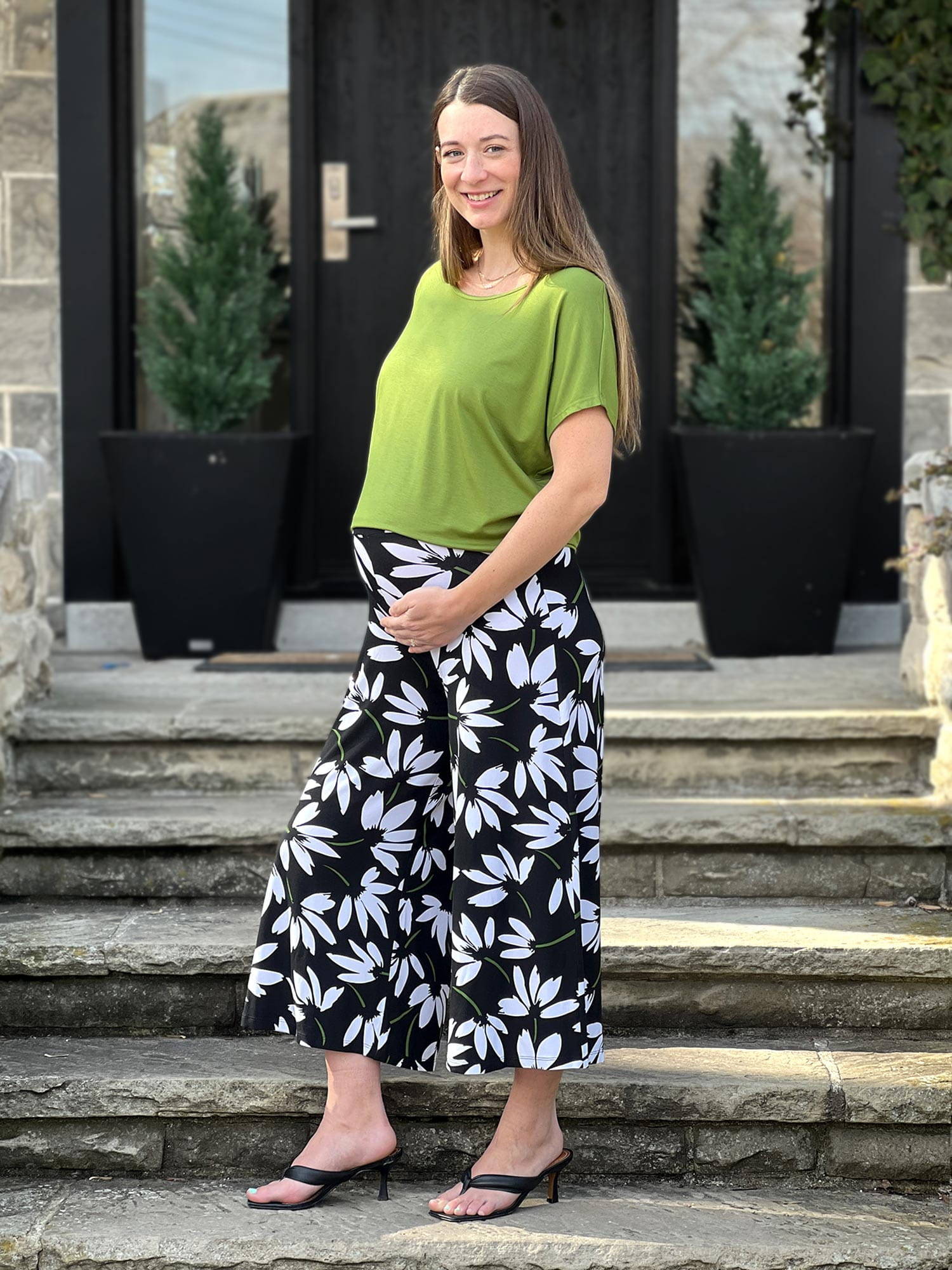 Pregnant woman standing wearing Miik's Keethai wide leg culotte in floral print with a green top.