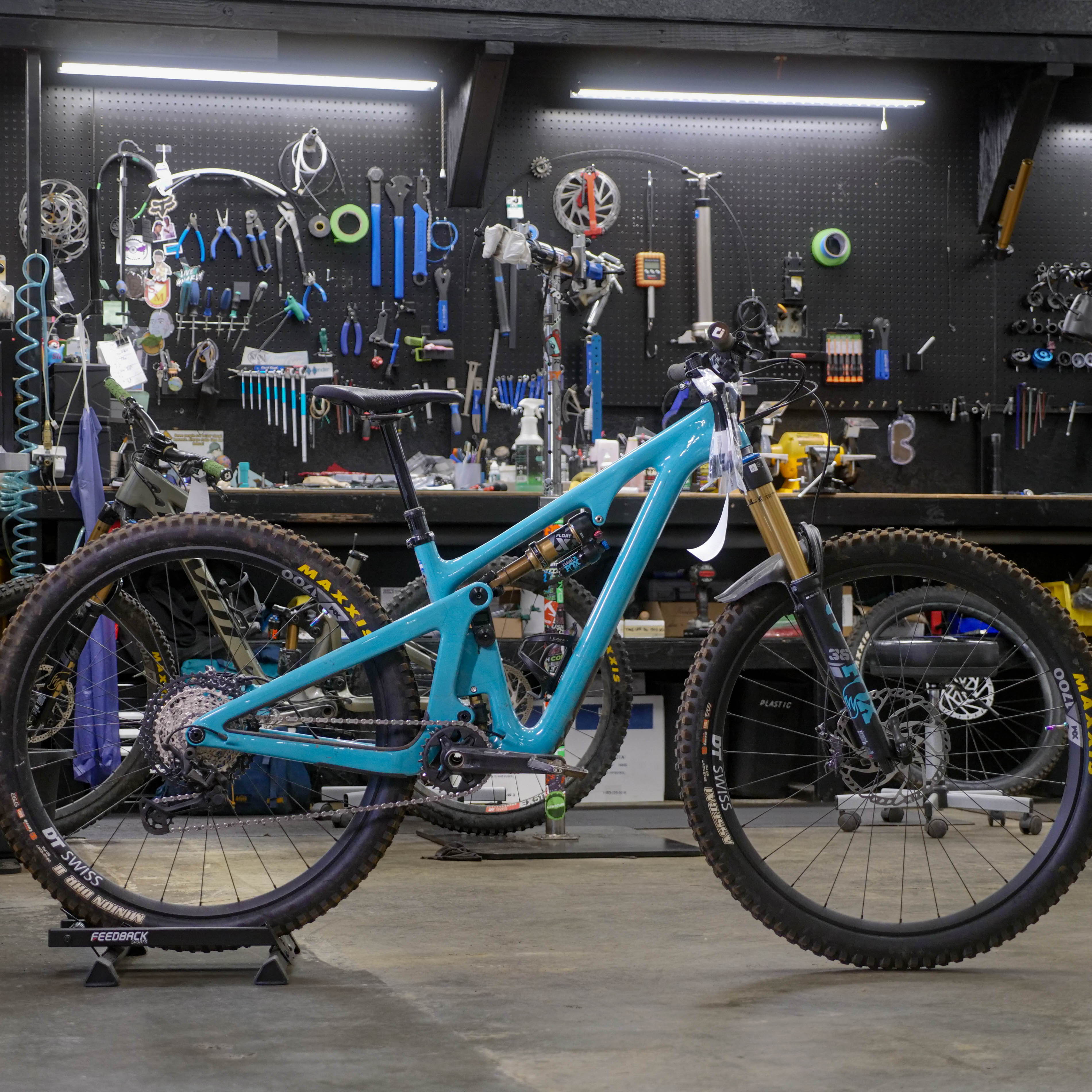 A blue mountain bike in a workshop with various tools in the background.