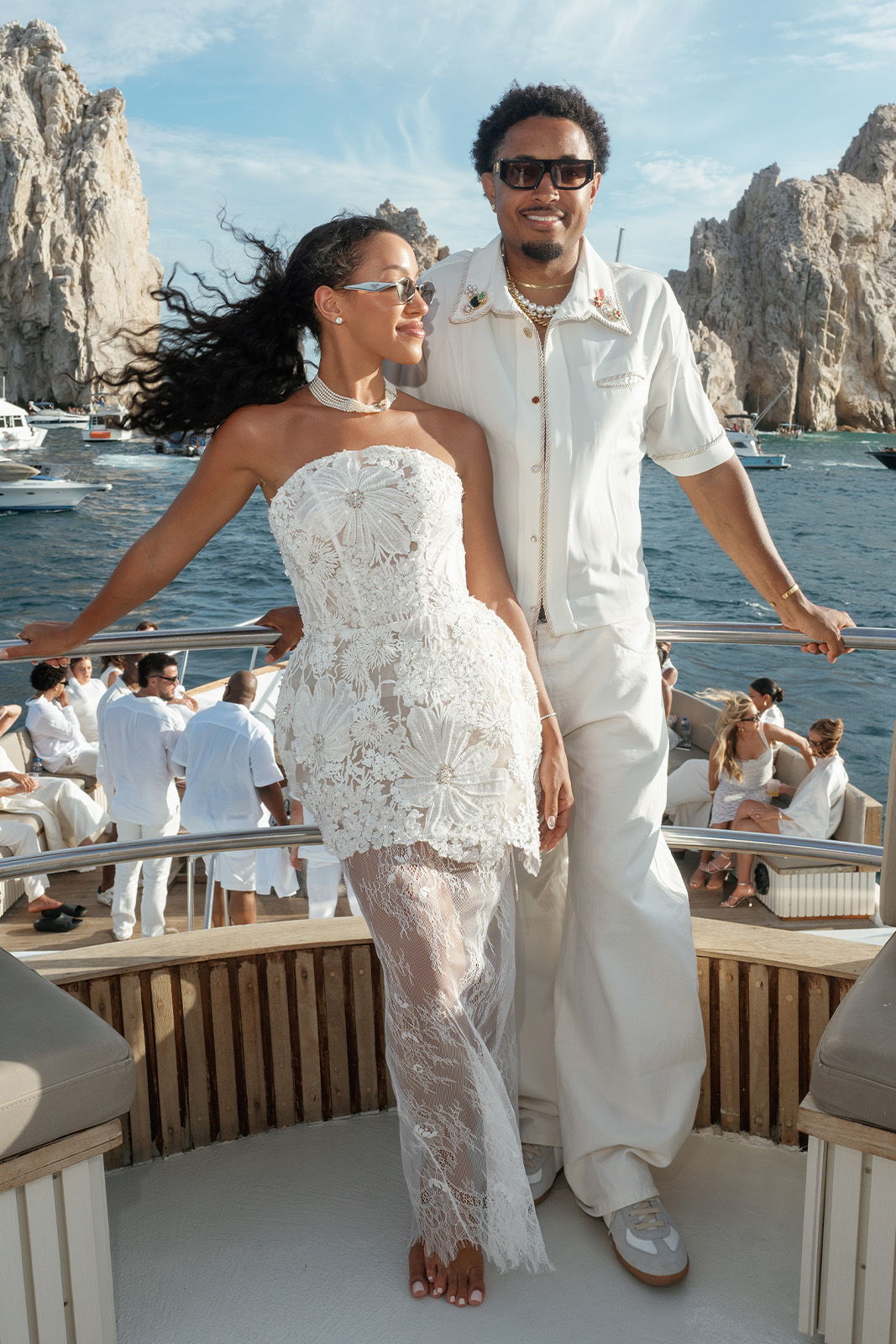 Couple posing on a yacht with ocean and rocky cliffs in the background.