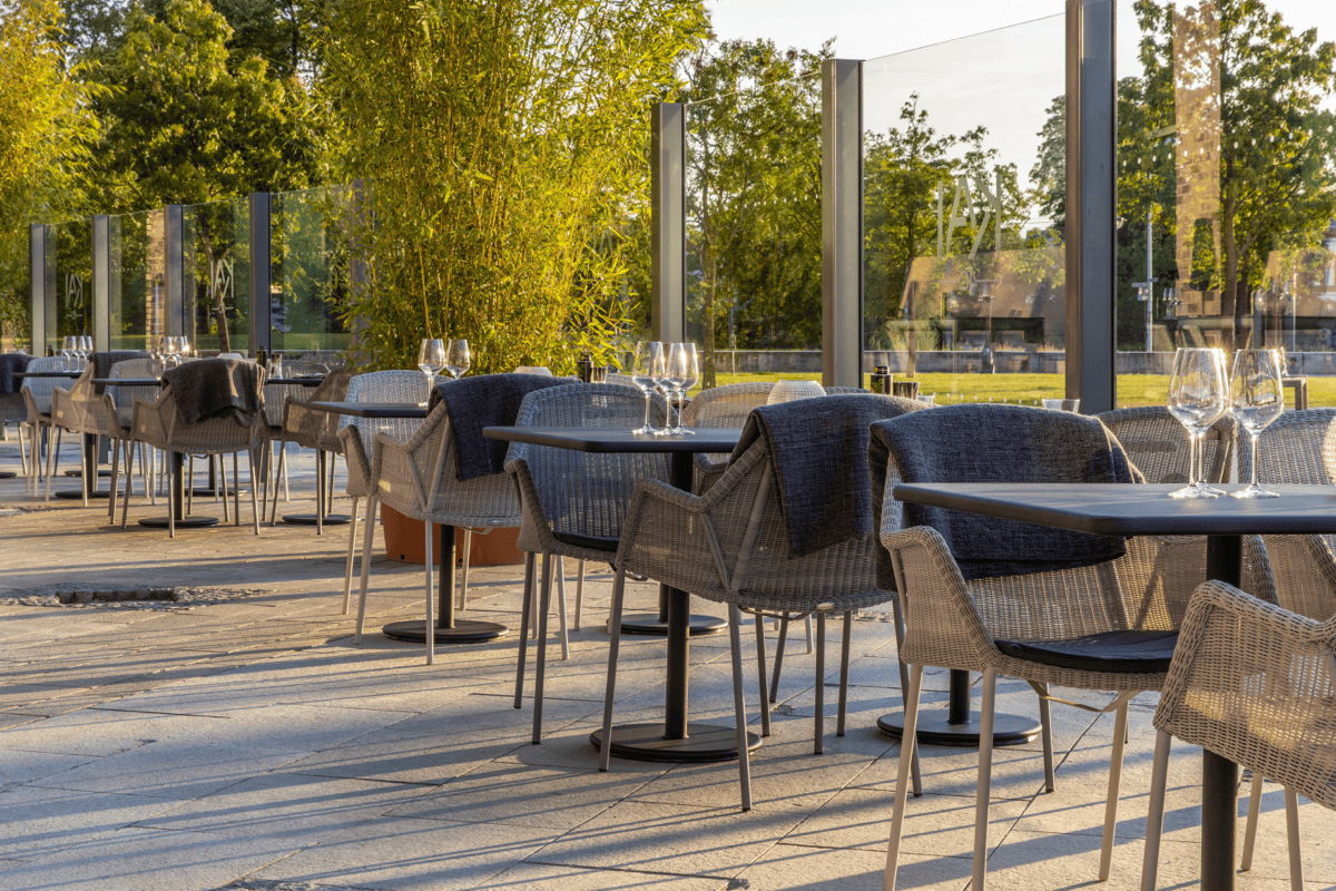 Outdoor restaurant dining area with durable commercial woven chairs, café tables and wind screens