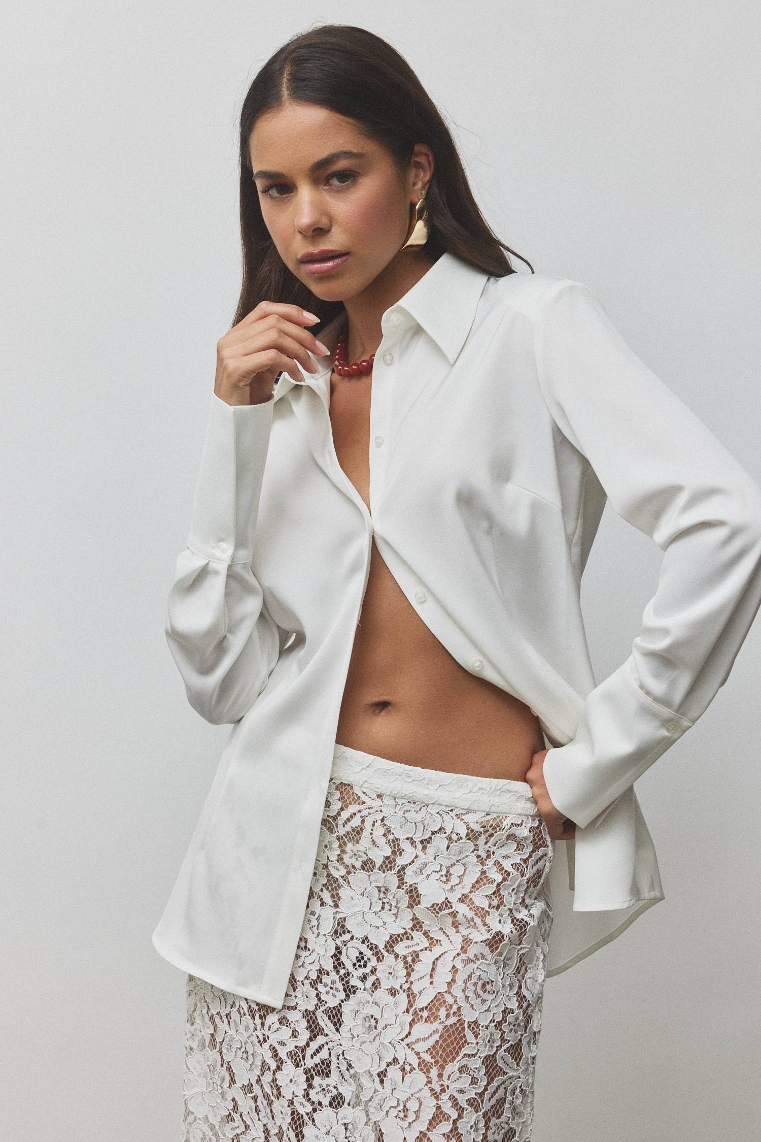 Model wearing a white shirt and lace skirt, posing confidently.