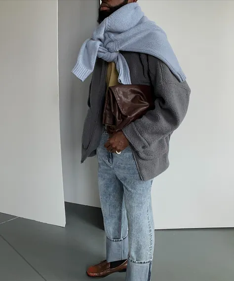 Person wearing a gray jacket, blue scarf, and holding a brown bag.