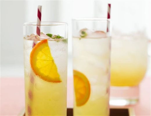Three drinks with orange slices and straws on a pink surface.