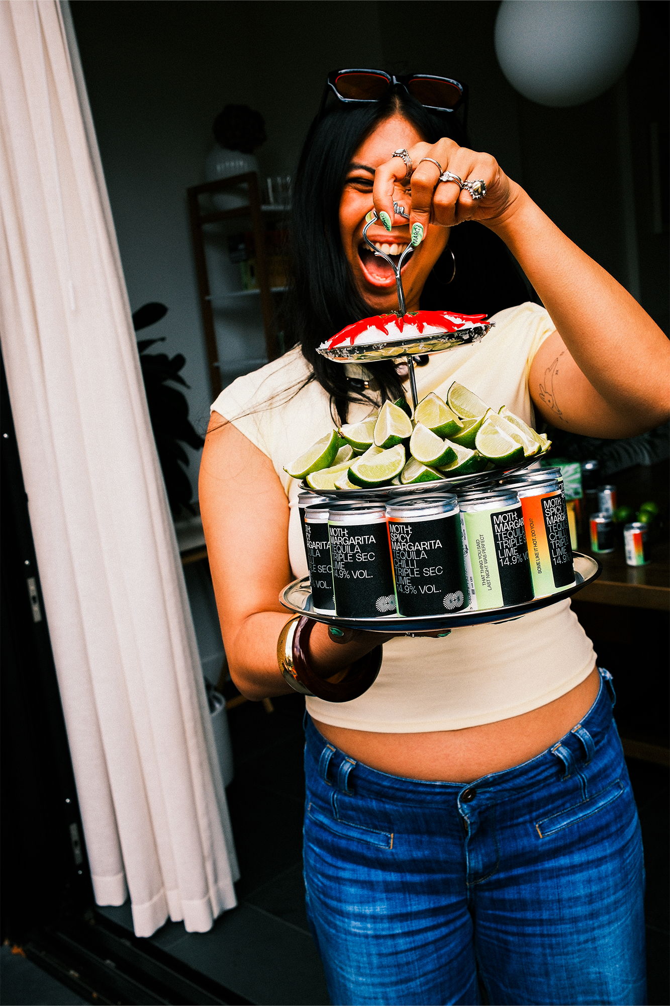 Person holding a tiered display of drinks and lime slices, smiling widely.