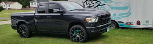 Ryan's dark gray 2019 Dodge Ram 1500 with turquoise brake calipers parked on a lawn beside a trailer