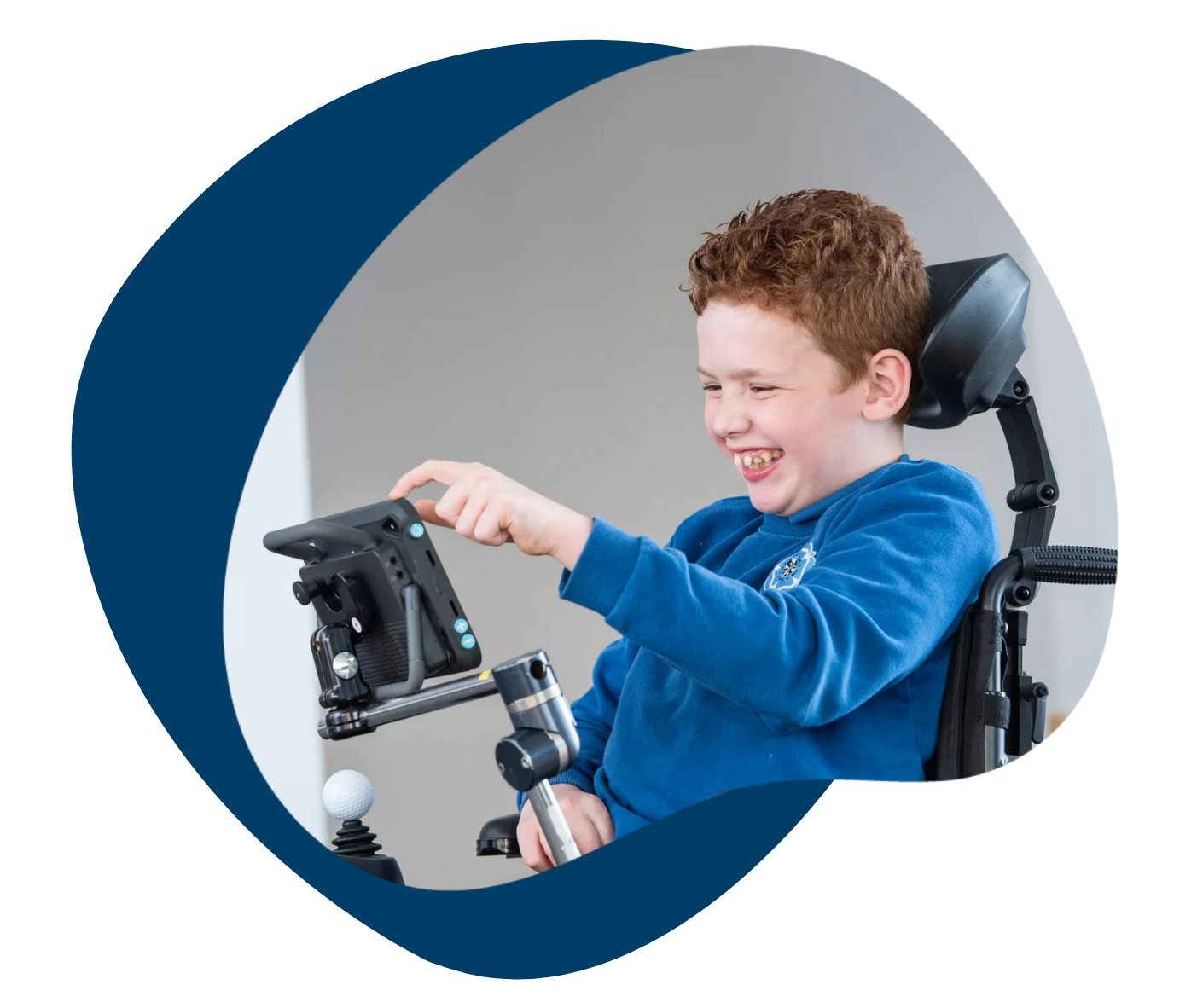 A boy in a wheelchair using a communication device, smiling happily.