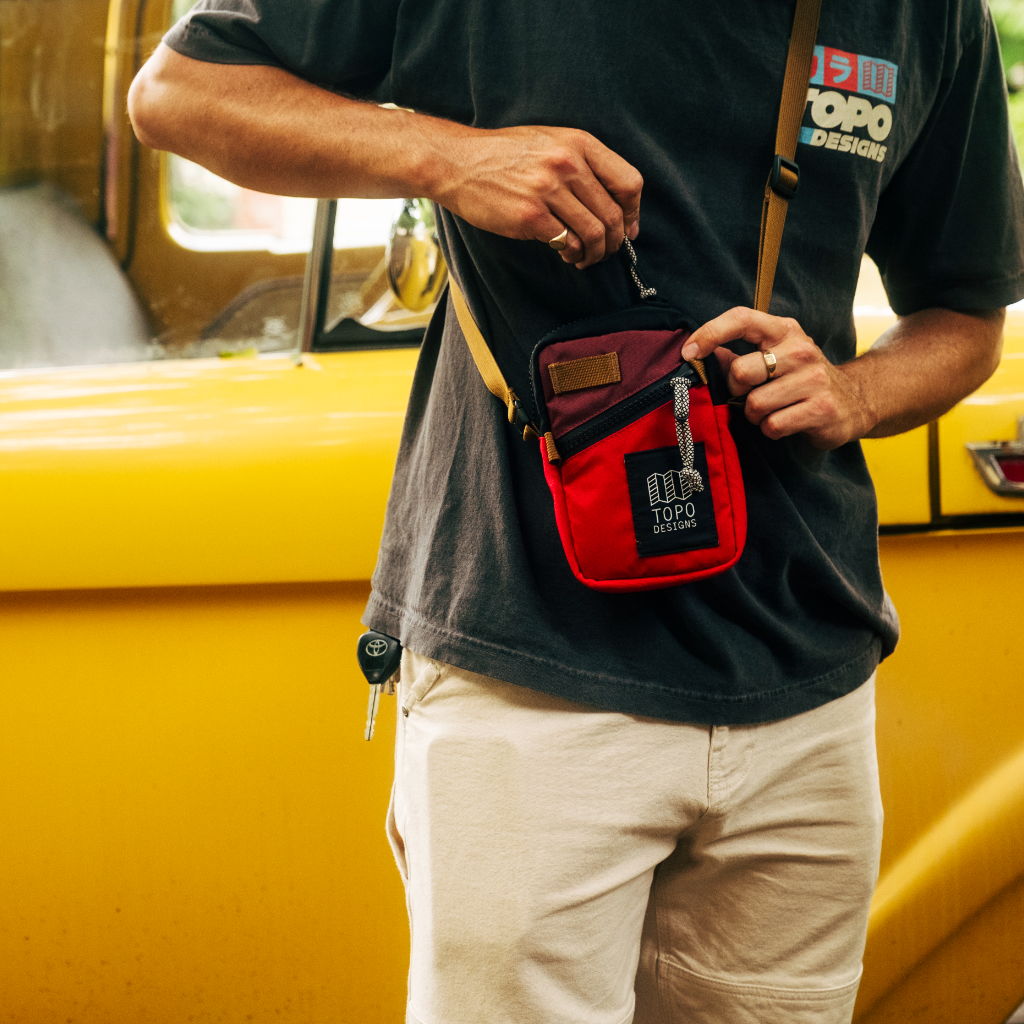 Person holding a small red bag near a yellow vehicle.