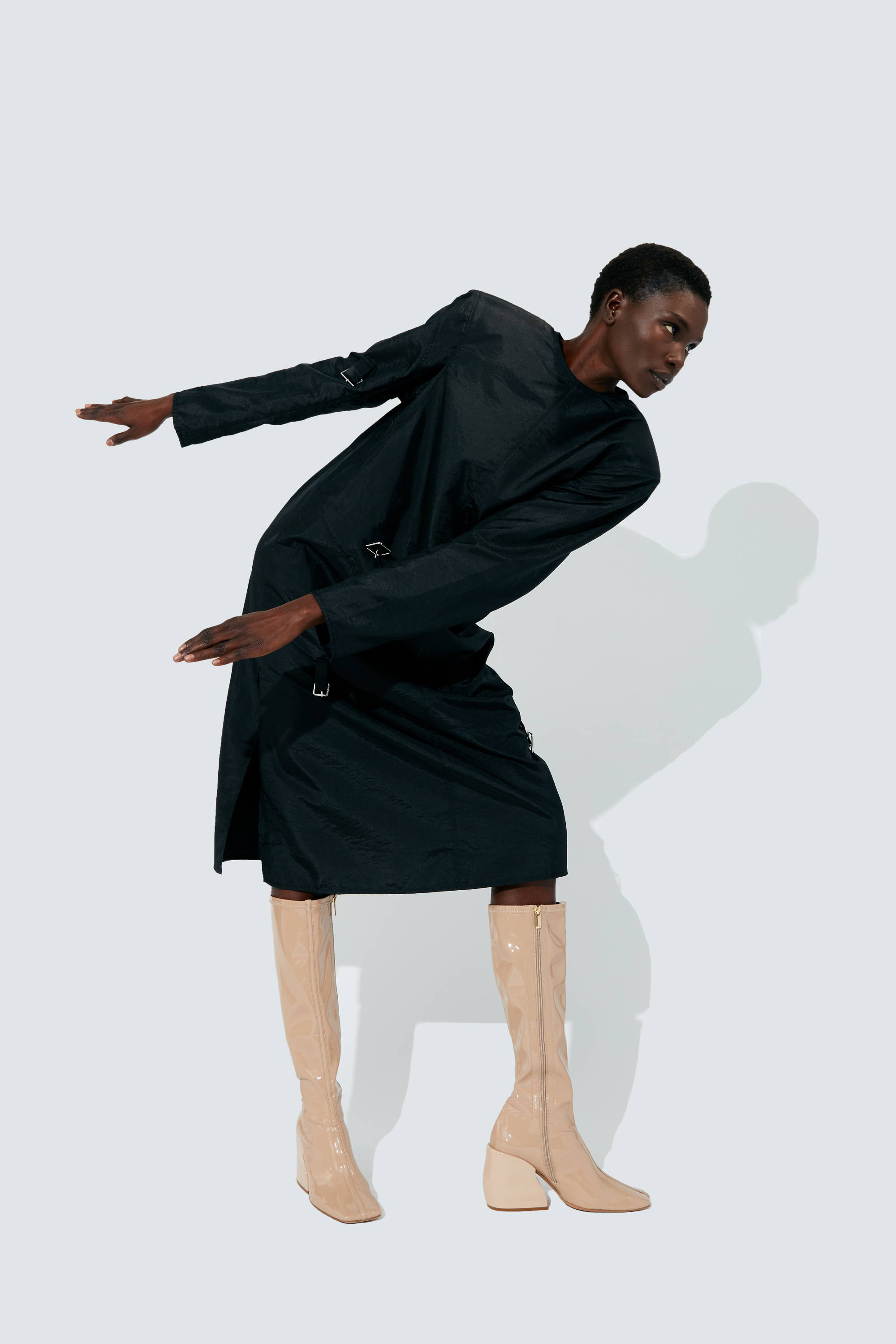 A person in a black dress and beige boots striking a dynamic pose.