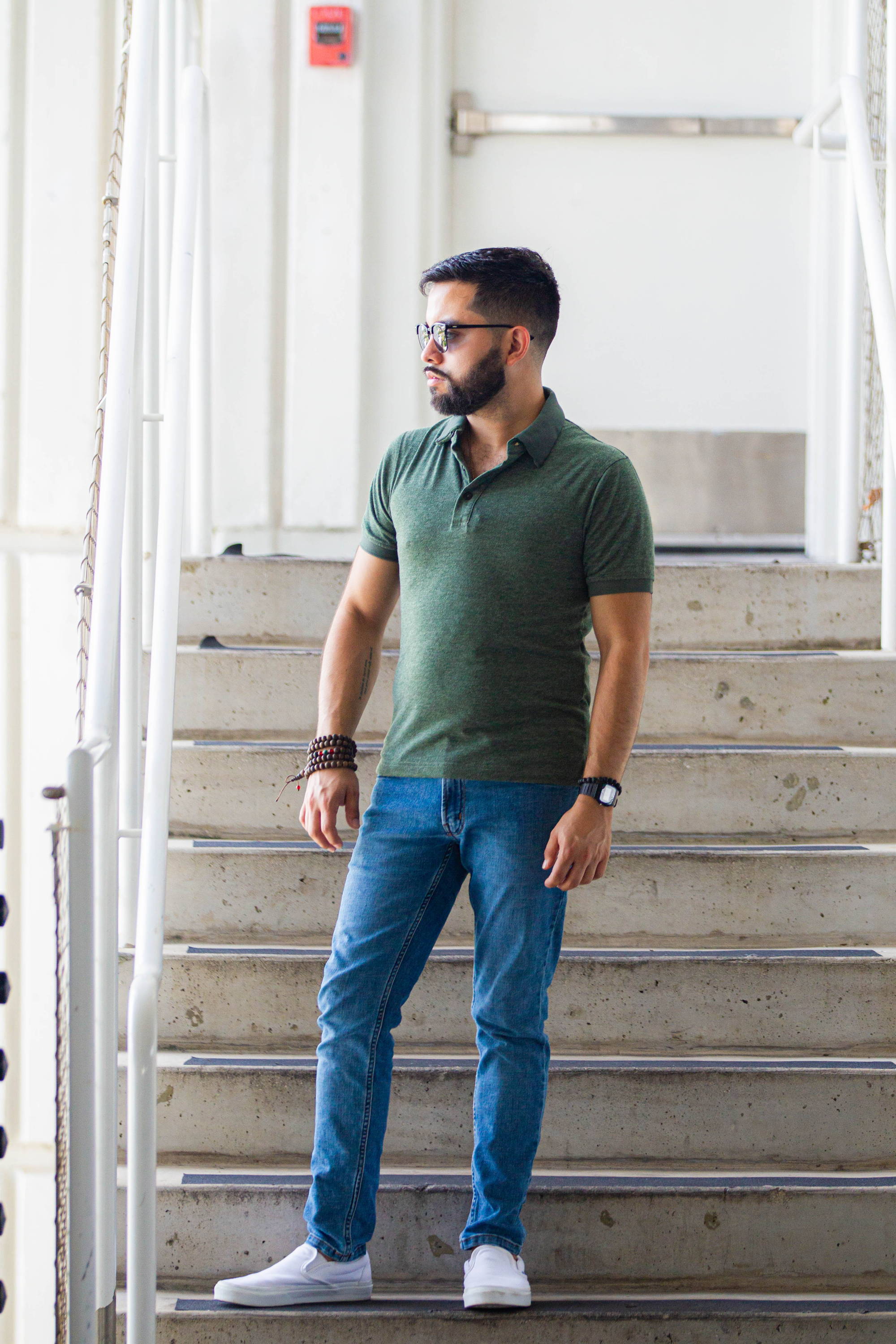Man standing in front of steps wearing white shoes, a green polo shirt, and light blue wash xavier jeans from under510.com