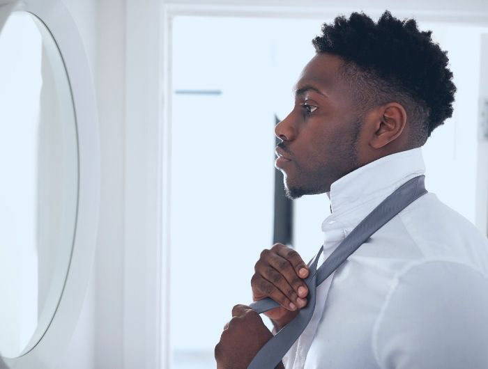 Man looking in mirror and tying a necktie