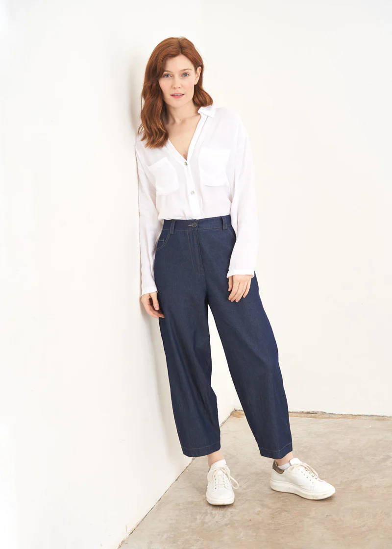 A model wearing a white shirt with a pair of dark blue chambray trousers and white trainers