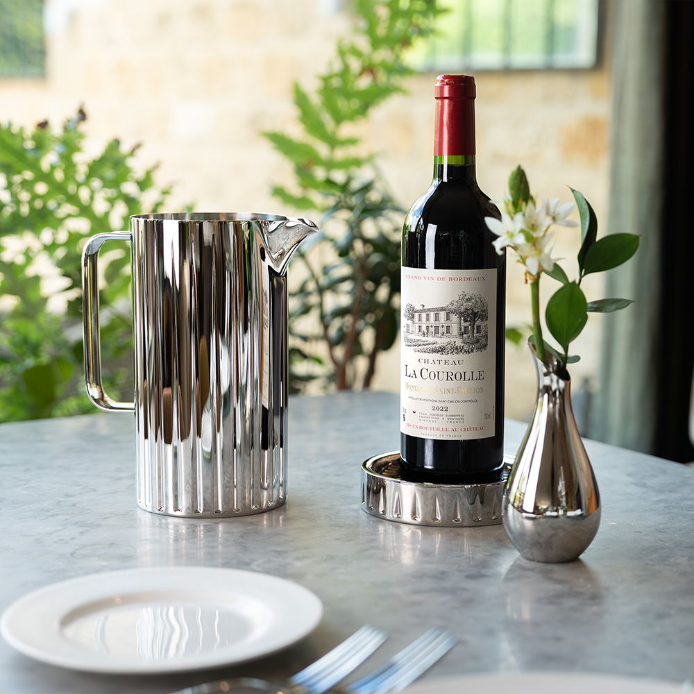 Dorset Pitcher, red wine bottle on the Dorset Coaster, and Drift Bud Vase on a table.