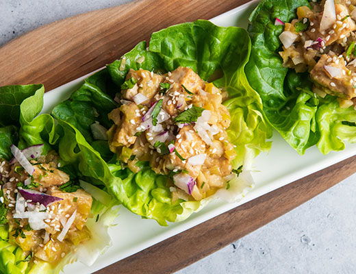 Three lettuce wraps filled with colorful ingredients on a white platter.