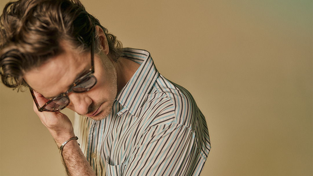 Person with glasses looking down, wearing a striped shirt against a soft background.