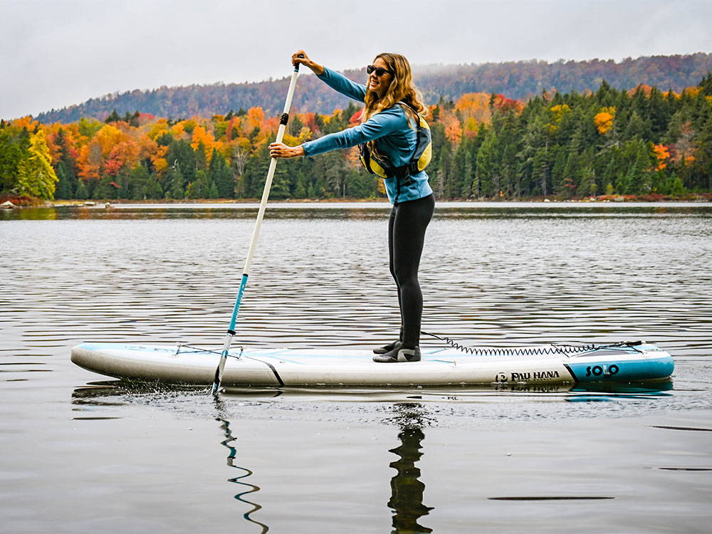 A woman paddling on a stand up paddleboard on a lake with autumn colors in the background