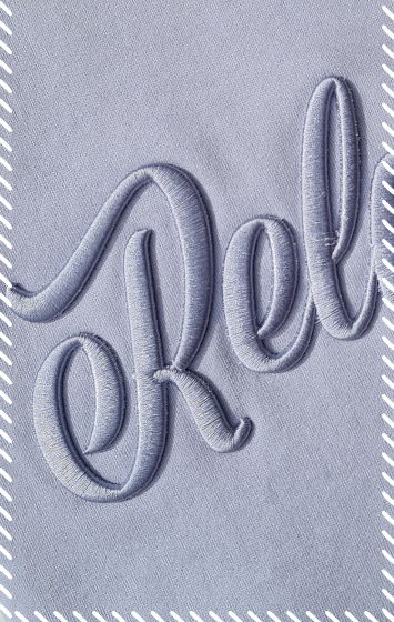 Close-up of tonal script logo embroidered onto powder blue fabric using raised with 3D puff embroidery stitching in matching powder blue thread