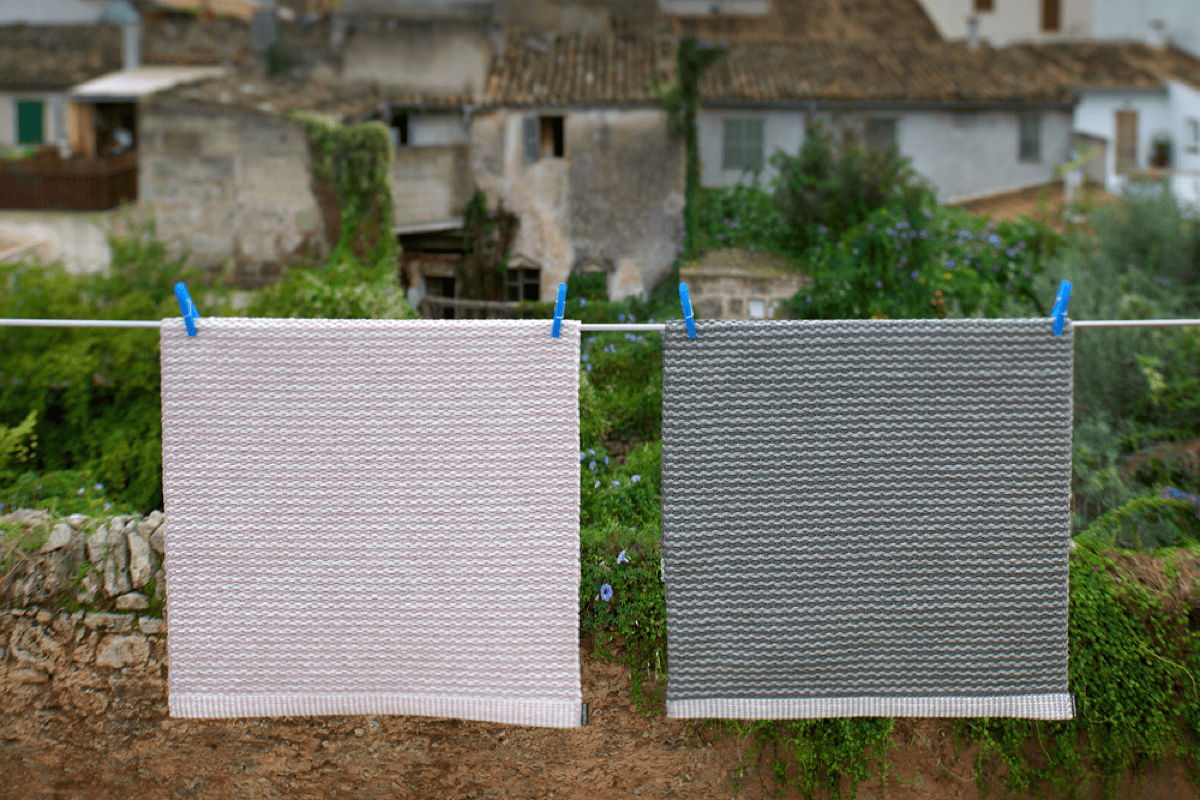 Two woven outdoor rug samples hanging on a clothesline outdoors, illustrating easy-care, washable patio rug materials designed for moisture resistance and durability.