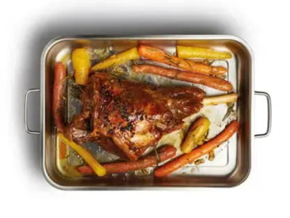 A roast leg of lamb in a silver roasting tin surrounded by carrots