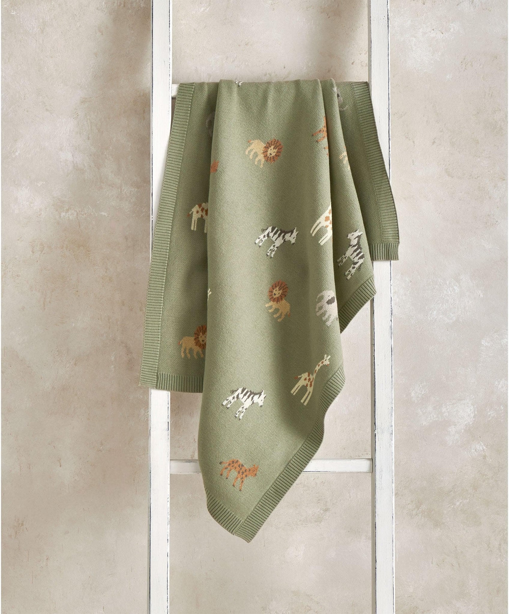 Embroidered animal-patterned blanket hanging on a white ladder.