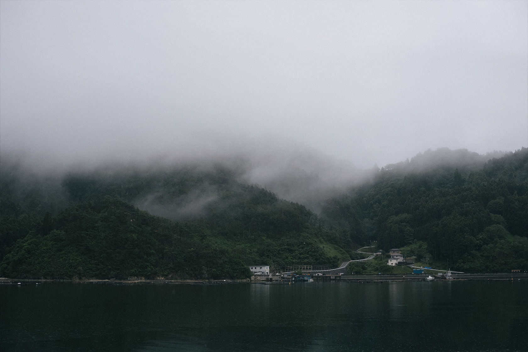 Foggy mountains reflected in calm water, with a small village visible.