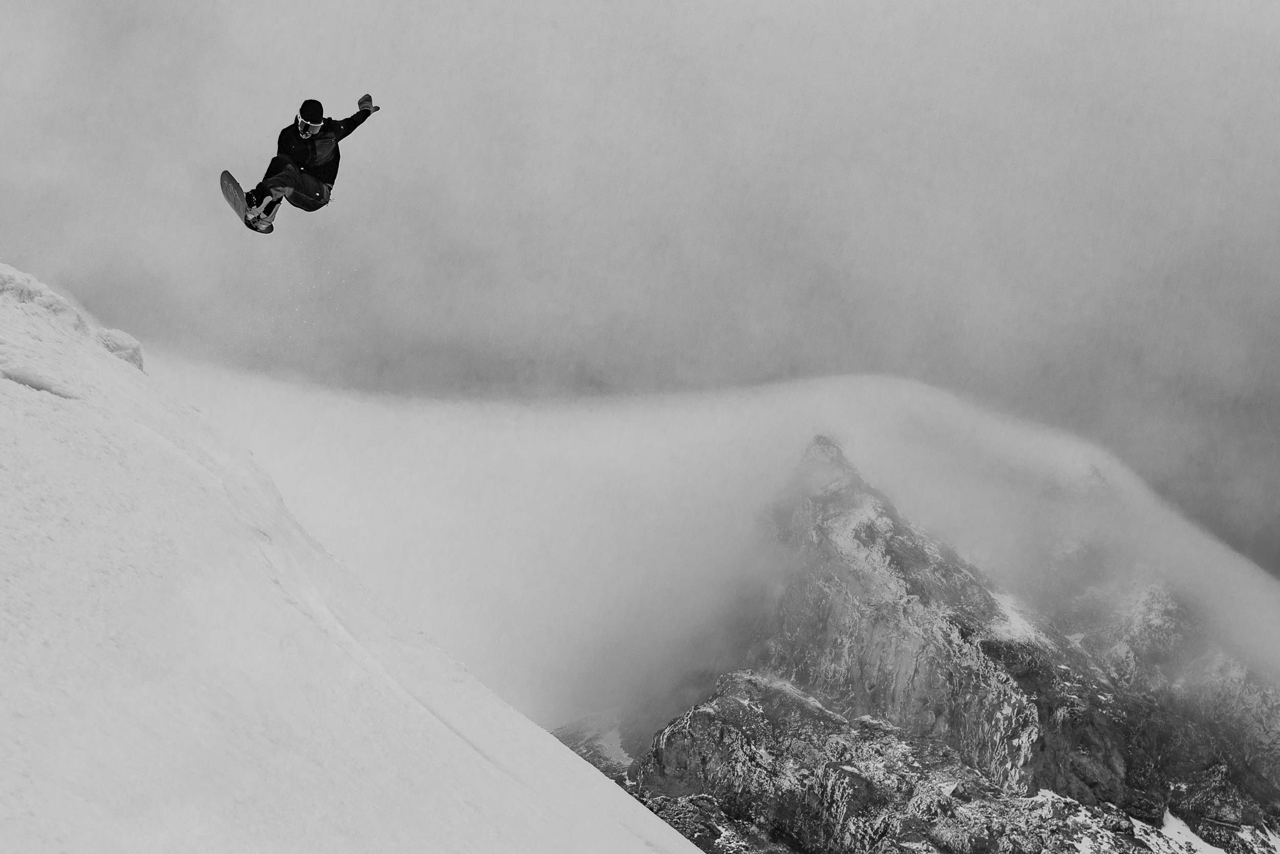 Snowboarder performing a jump in a snowy, mountainous landscape.