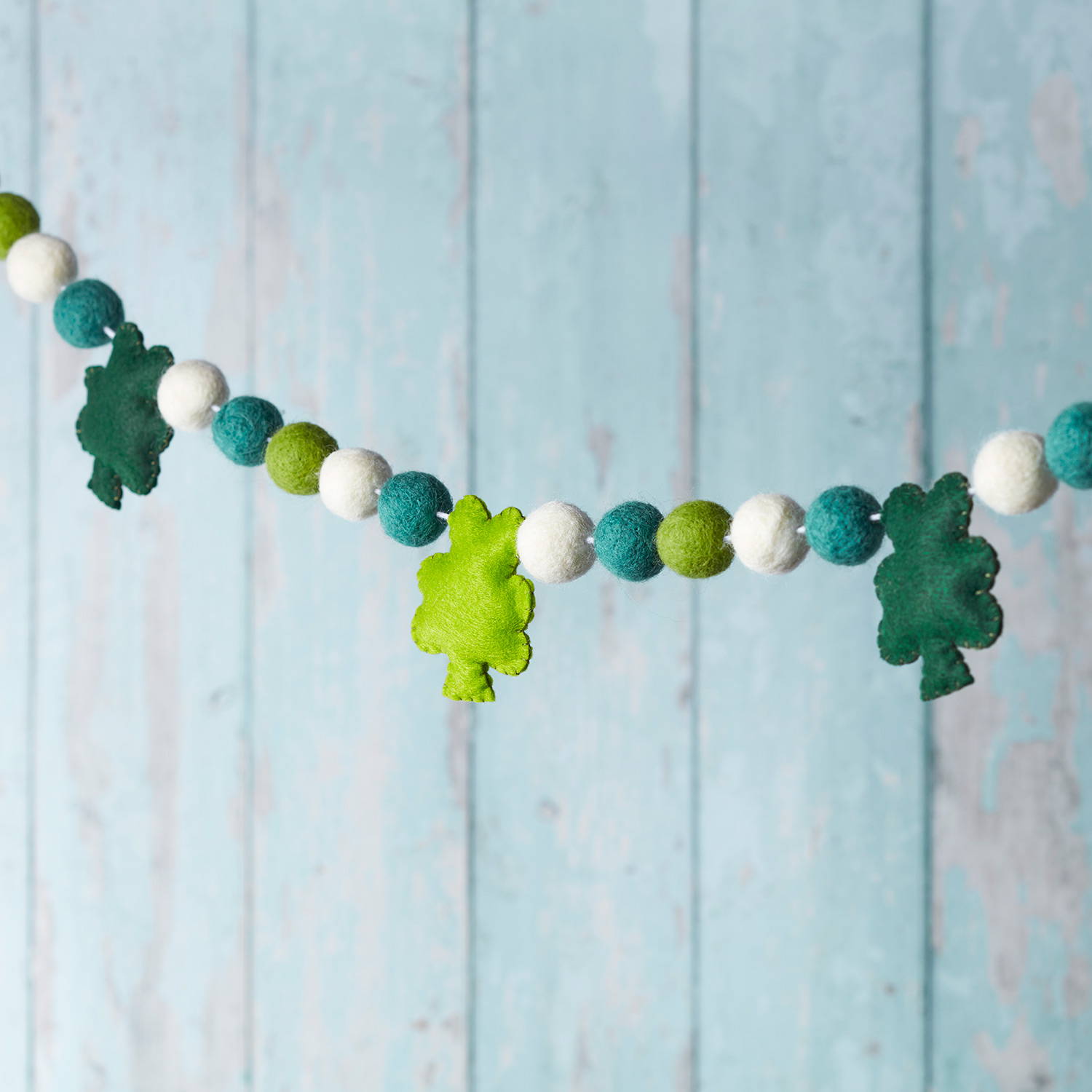 Felt green shamrock decoration hanging in front of a blue wooden rustic wall.