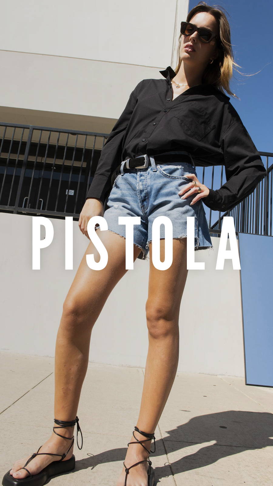 Woman in black button up and Pistola jean shorts modeling in front of a concrete wall