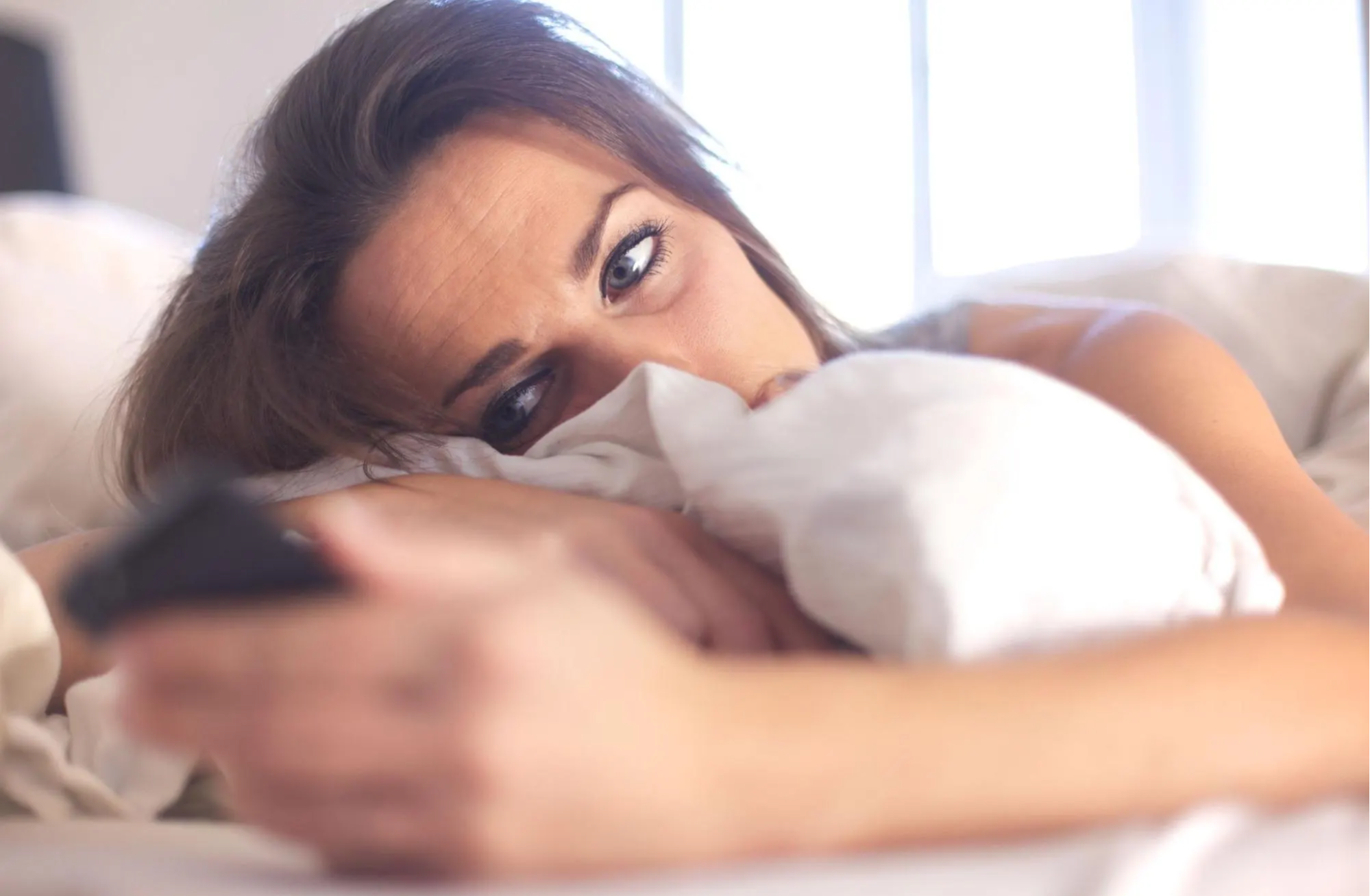 woman laying in bed holding cellphone