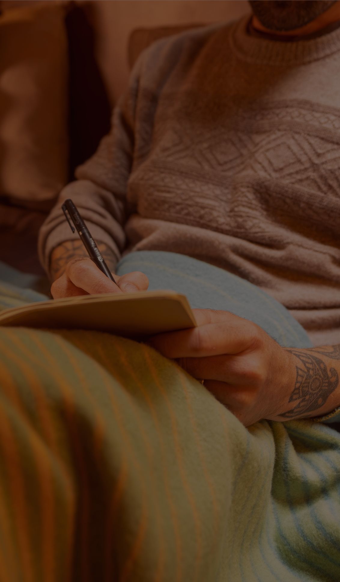 Person writing in a notebook while sitting under a colorful blanket.