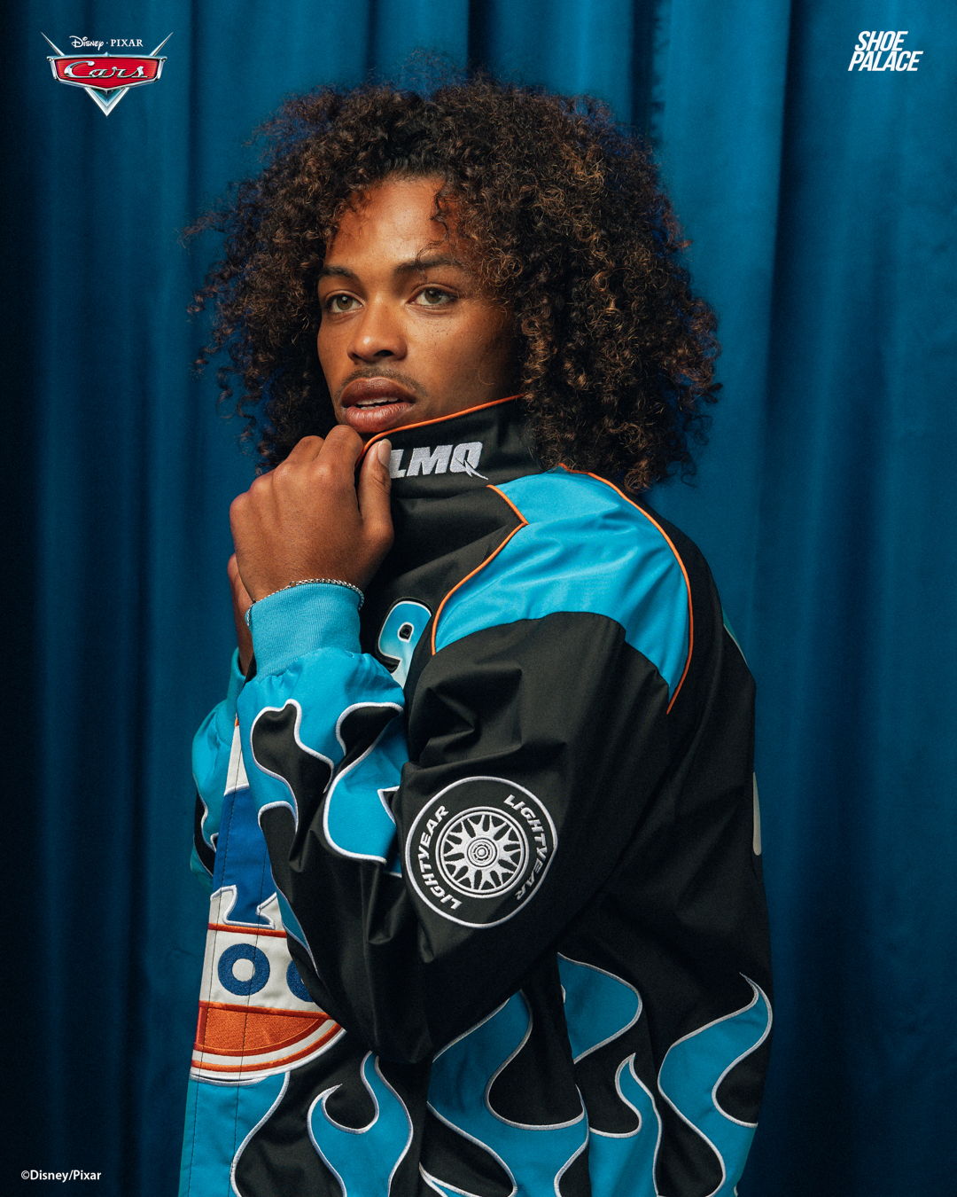 Person with curly hair wearing a blue jacket against a blue backdrop.