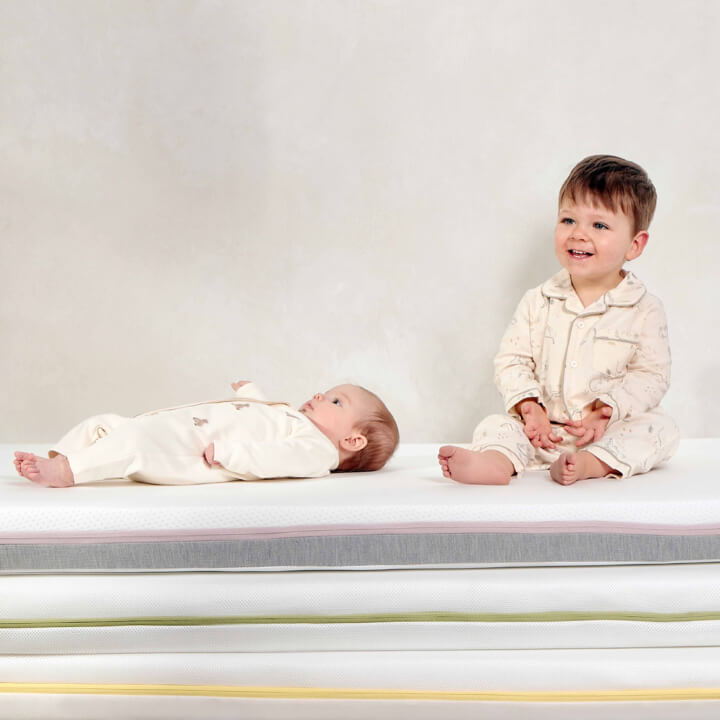 Two children in pajamas, one sitting and one lying down on a mattress.