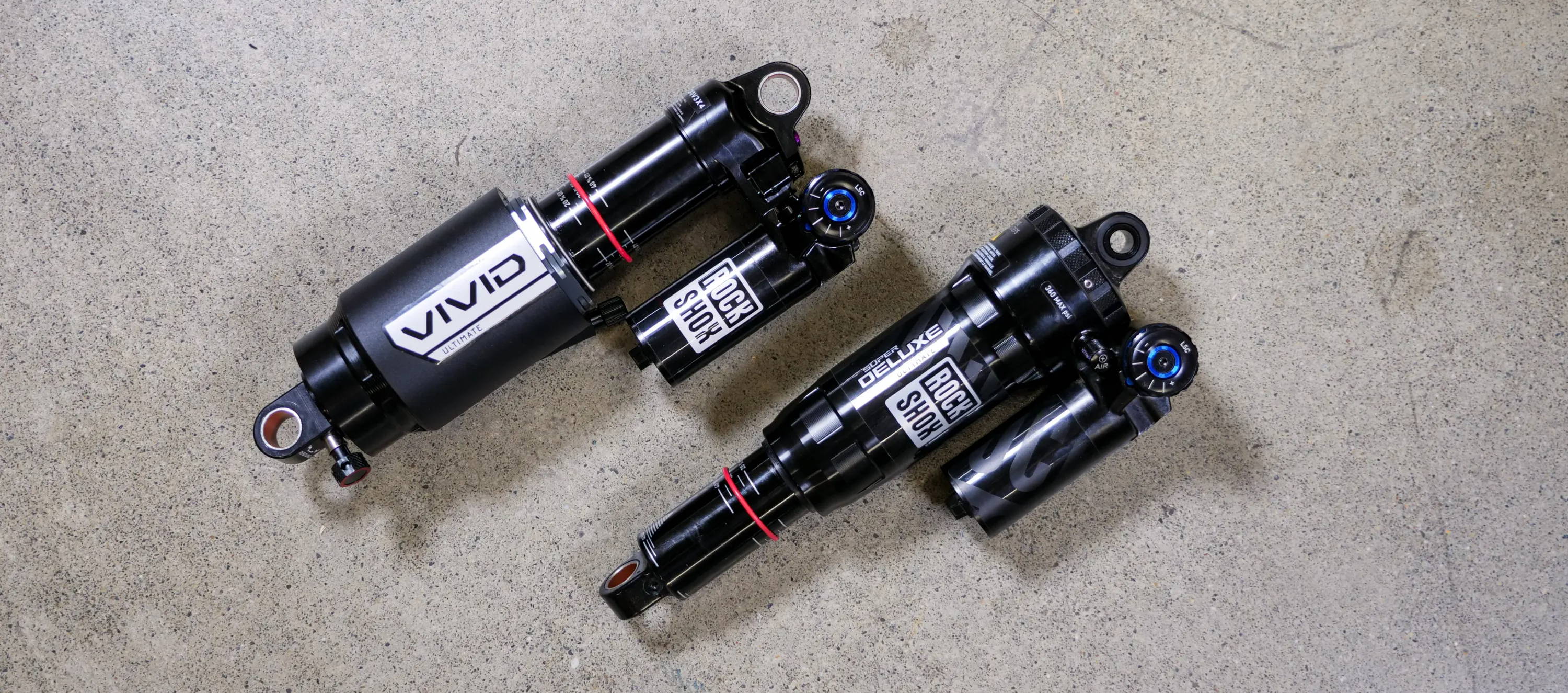 rockshox super deluxe ultimate and vivid rear mountain bike shocks laying on concrete to be compared