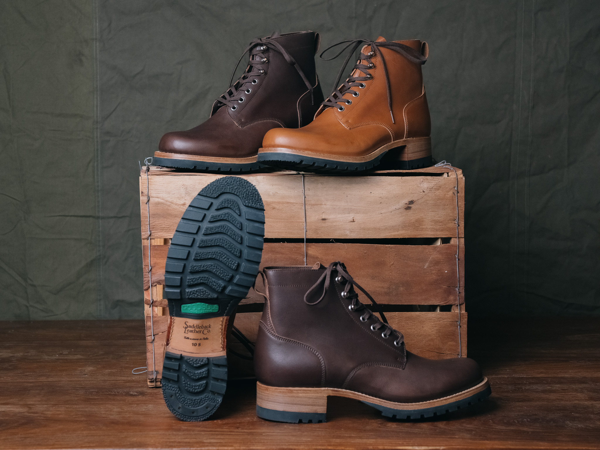 Brown and tan boots displayed on a wooden crate with a green background.