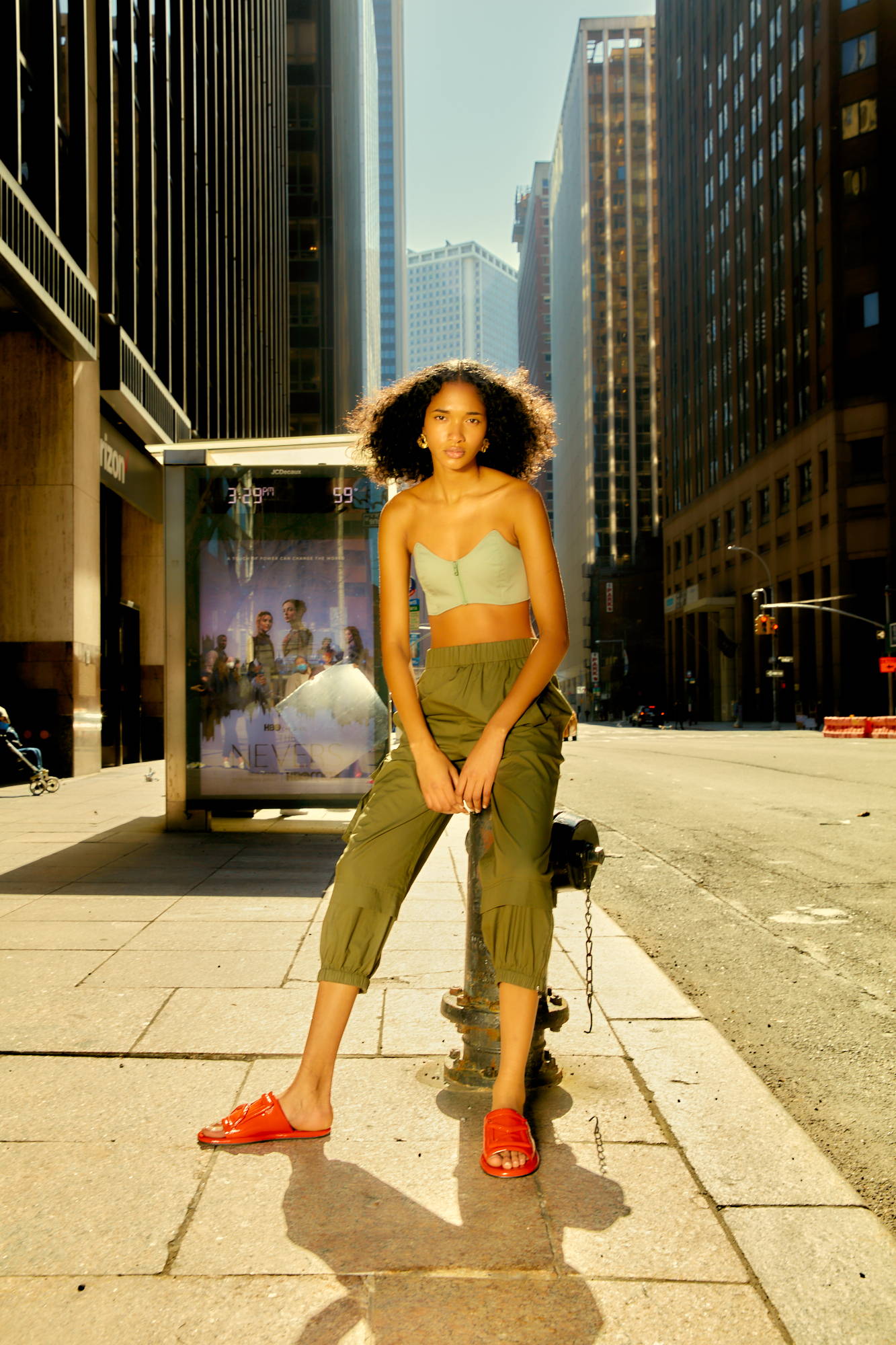 Model in casual outfit standing on a city street with buildings in background.