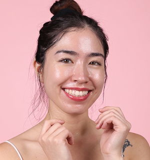 Smiling woman with a bun hairstyle against a pink background.