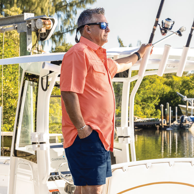 Man standing on boat overlooking water wearing Seacliff 2.0 short sleeve shirt in coral color.