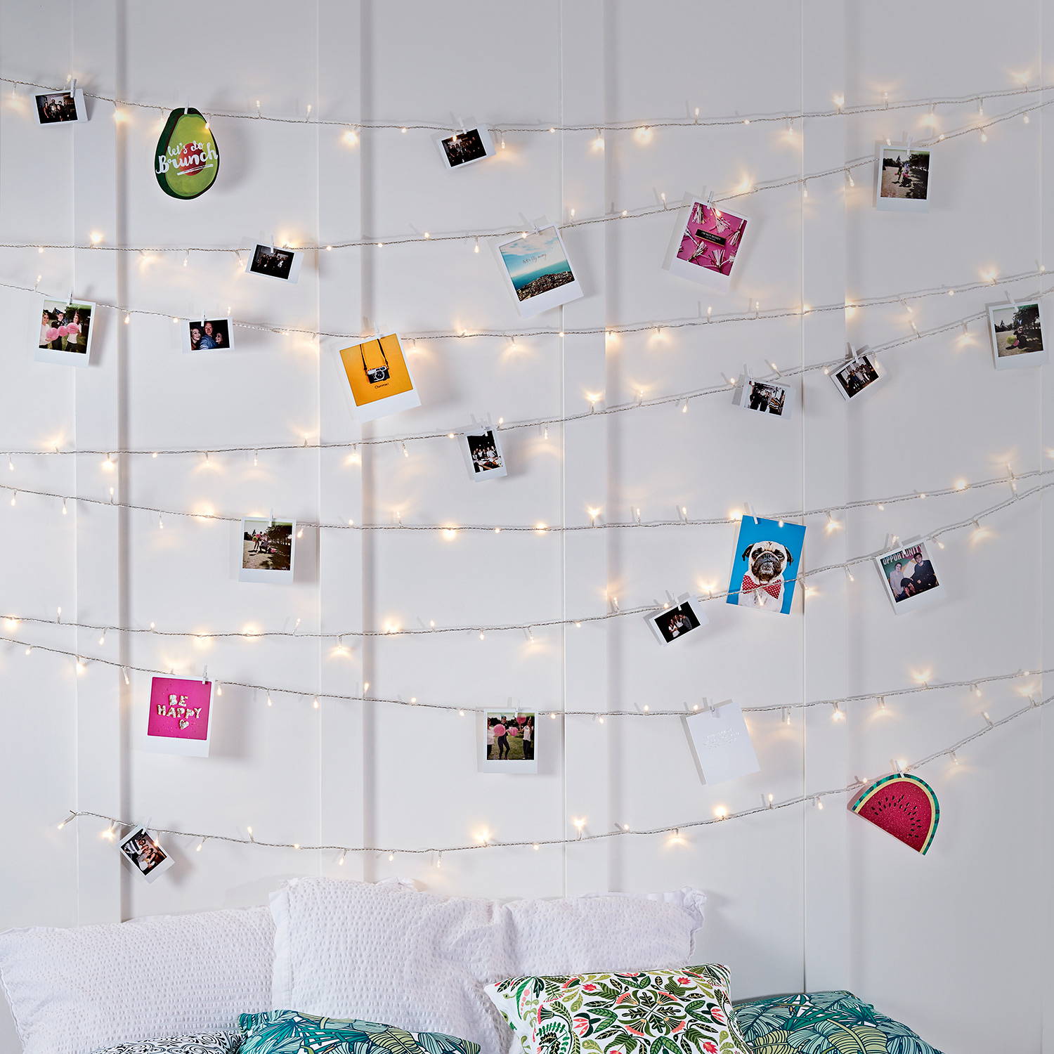 Warm white fairy light wall with photos attached above a cosy bed.