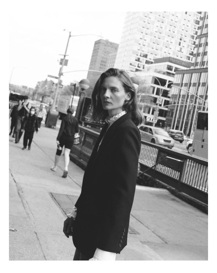 A person with long hair wearing a black blazer on a city street.