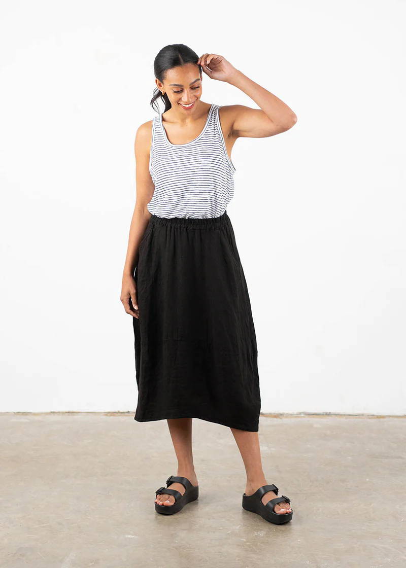 A model wearing a sleeveless, blue and white striped vest with a black linen tulip midi skirt and black chunky slides