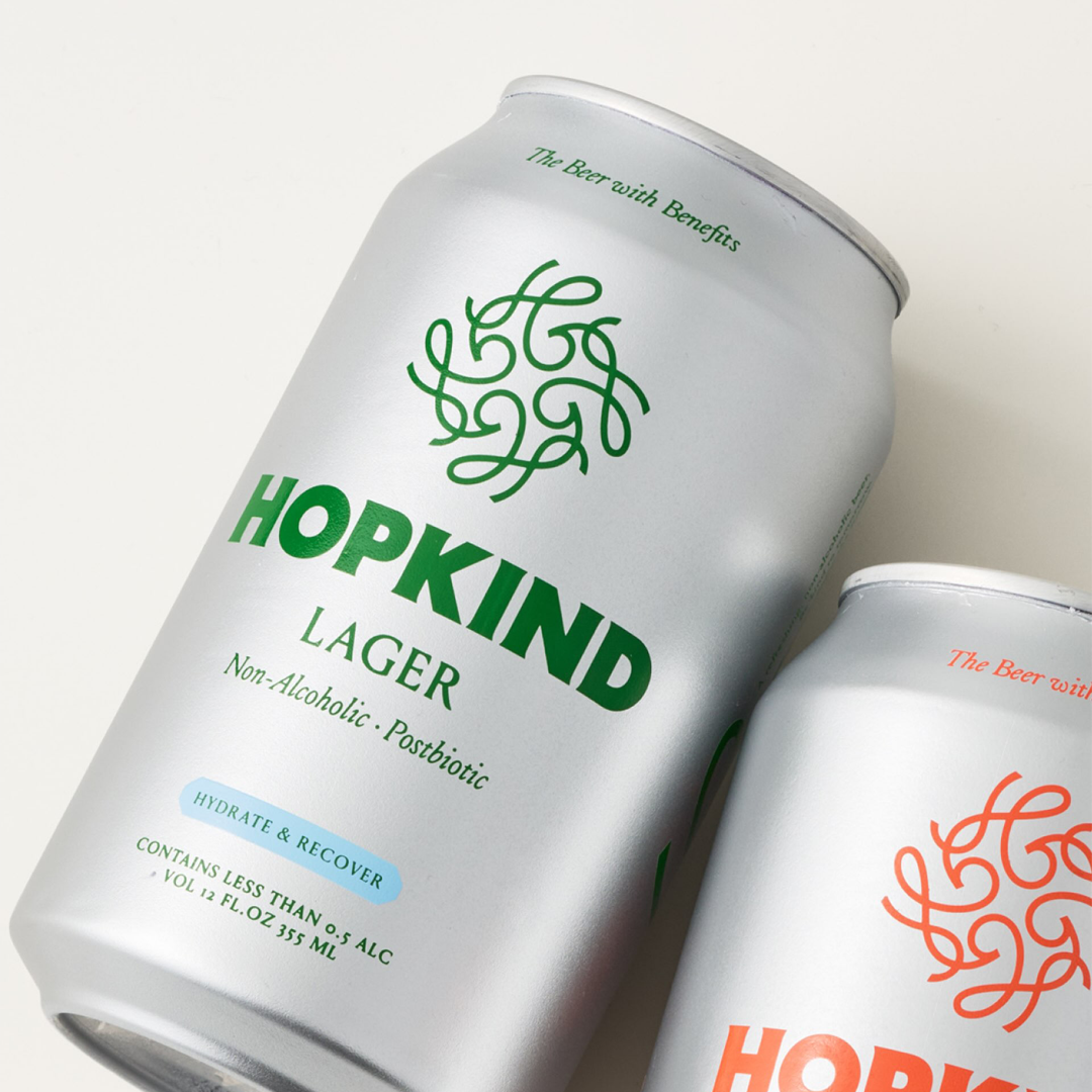 Two cans of Hopkind Lager, one green and one orange logo.