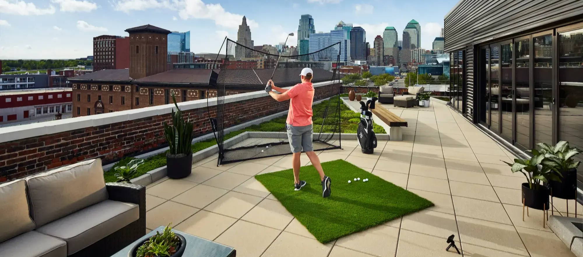 A golfer hitting balls into a practice net using a golf launch monitor on a rooftop
