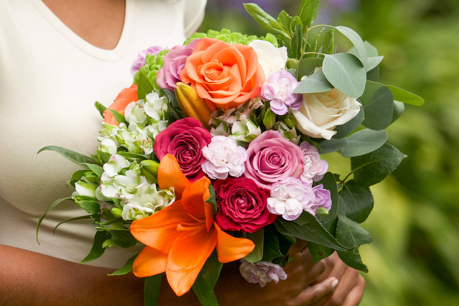A woman holds a bright bouquet with orange and lilac roses, orange lilies,  white Charmelia and other spring varieties 