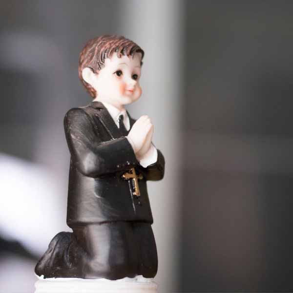 Cake topper of a boy wearing a black suit and praying