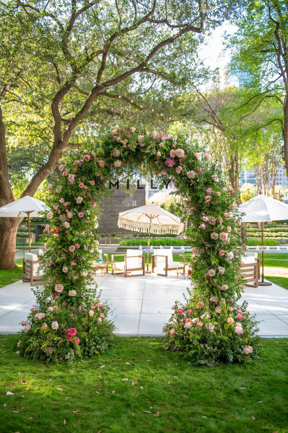 Floral archway in a garden setting with seating and umbrellas.