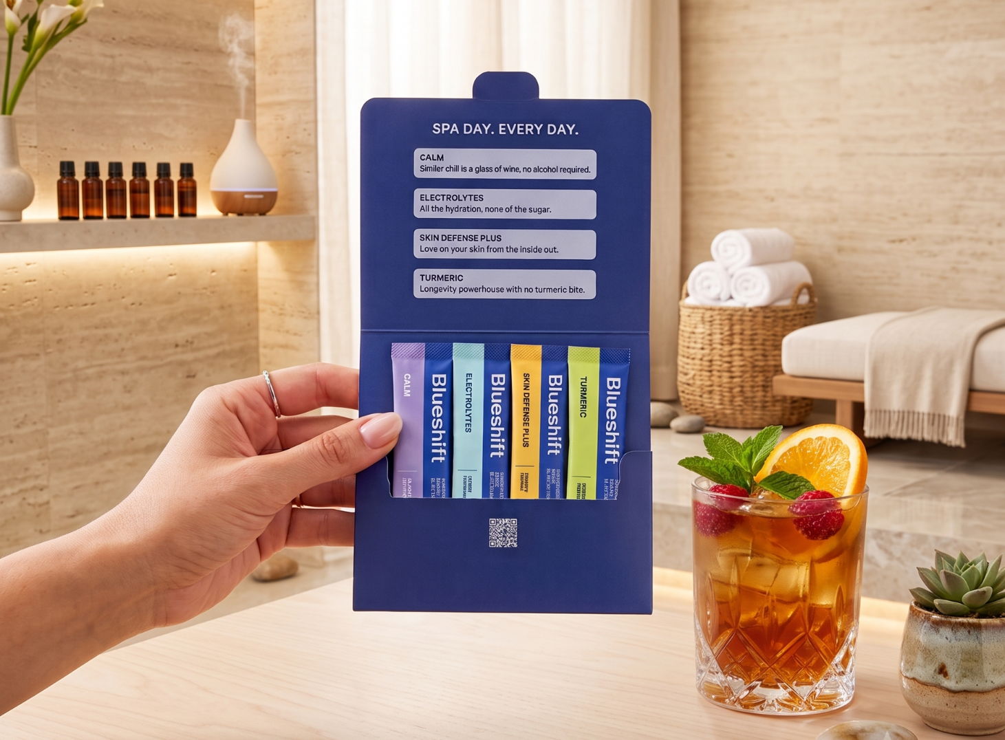 A woman holding the Mind + Body Reset Kit over a table in a spa setting, with a prepared drink behind it, garnished with fresh fruit.
