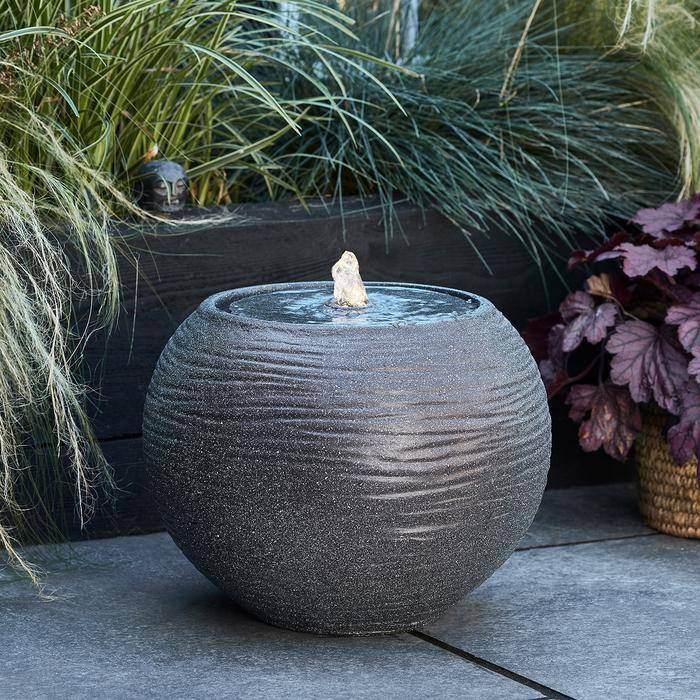 A round grey water feature as part of a relaxing garden display.