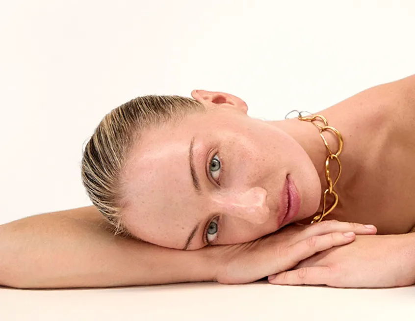 A woman resting her head on her hands, wearing a gold necklace.