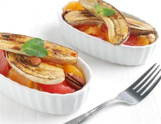 Two small dishes of baked fruit topped with banana and mint.