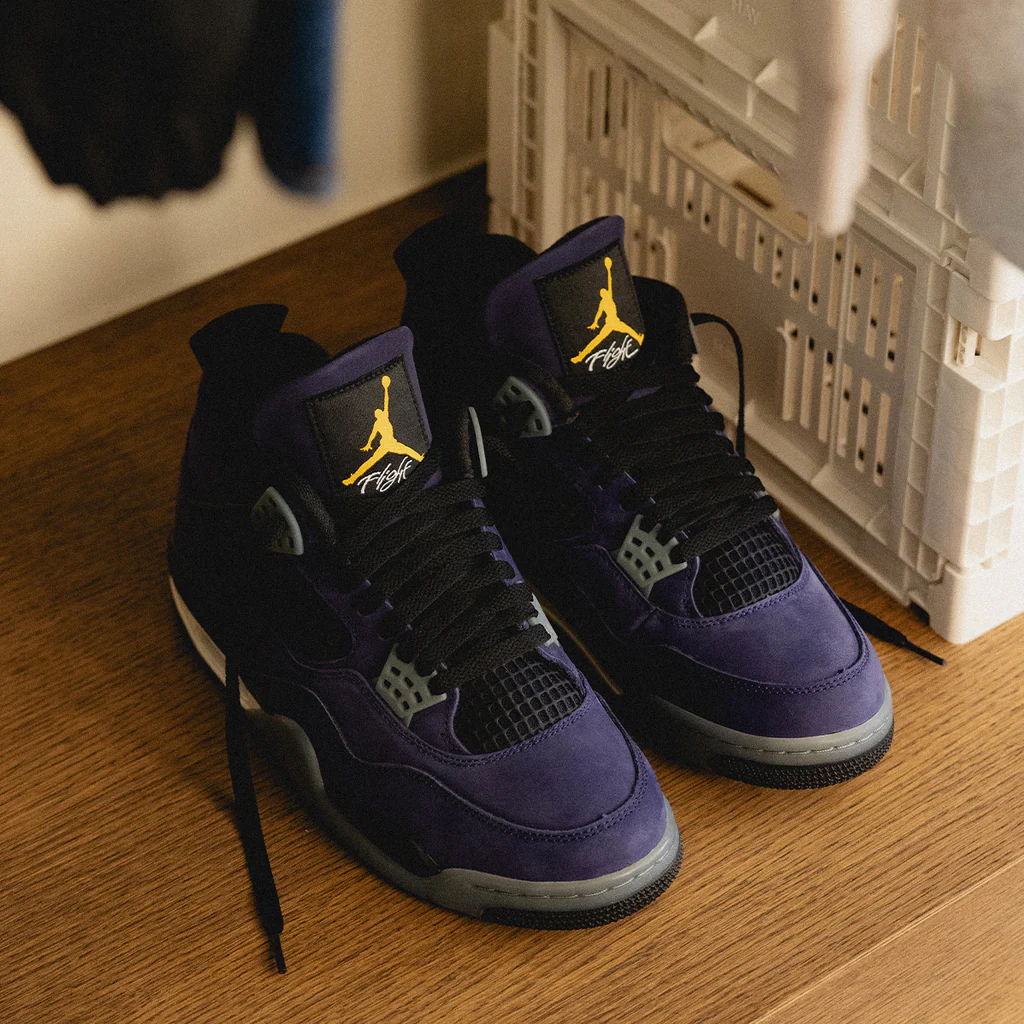 A pair of purple and black Air Jordan 4 sneakers on a wooden floor.