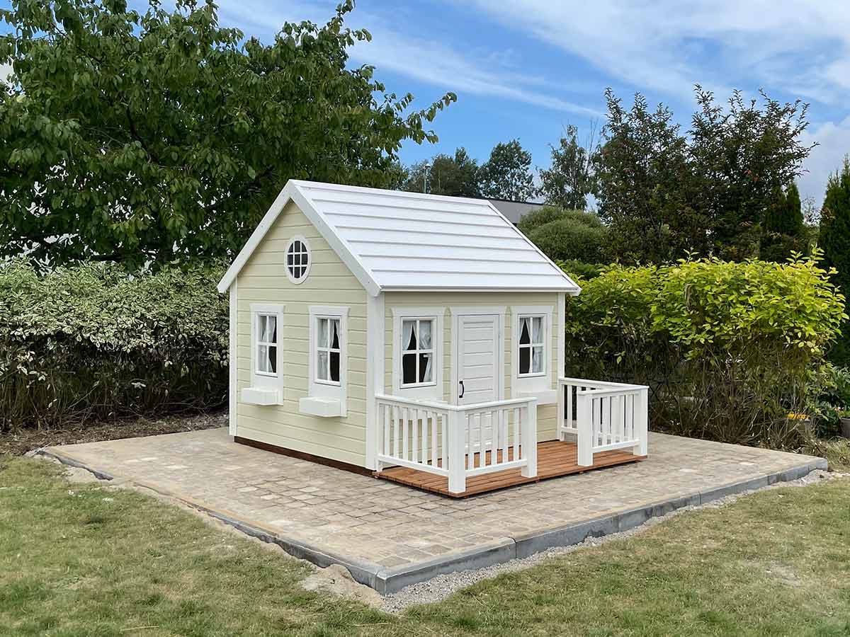 Custom playhouse in light color in a cargen on a stone ground by WholeWoodPlayhouses